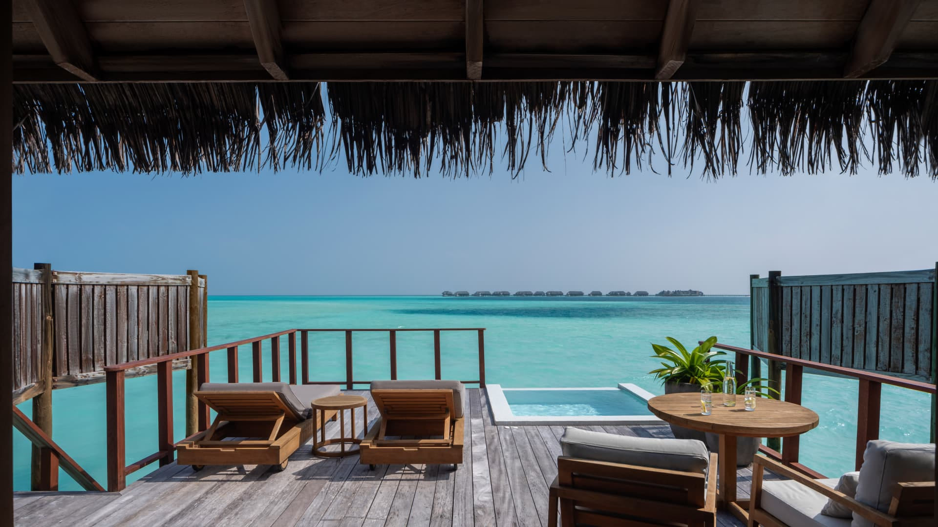 Blick von der privaten Terrasse einer Overwater Villa im Conrad Maldives Rangali Island auf den türkisblauen Indischen Ozean mit Infinity Pool und Sonnenliegen.